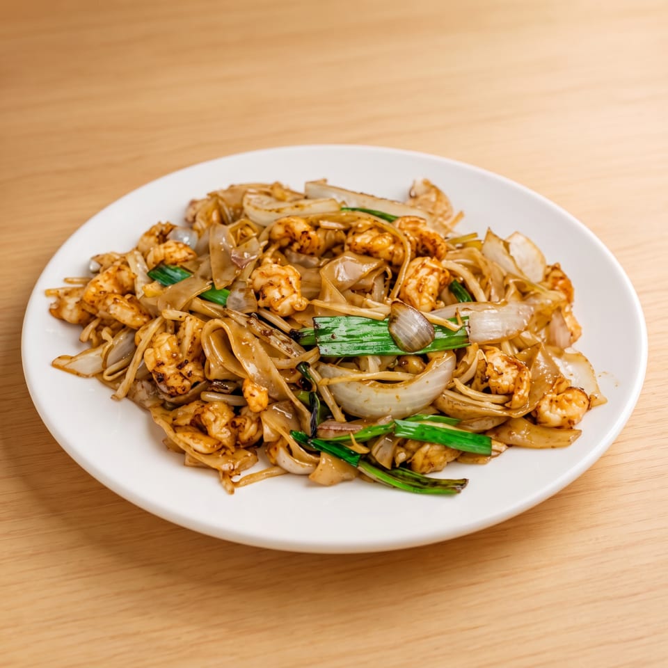 Shrimp and wide rice noodles stir-fried with onions and green scallions on a white plate.