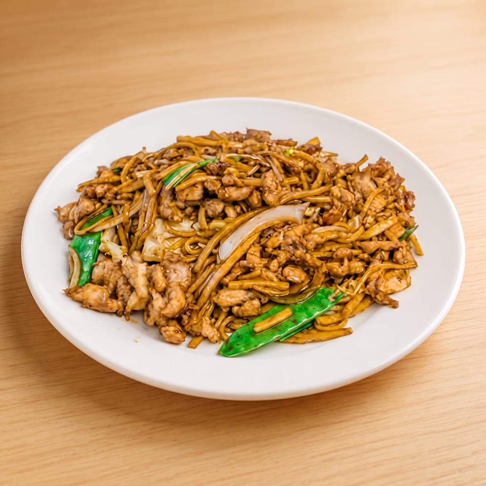 Chicken lo mein with noodles, onions, and green snap peas on a white plate.