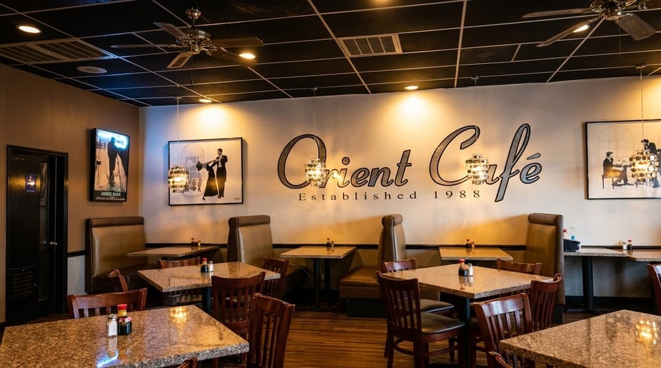 Interior of Orient Cafe with dining tables, booths, and a large "Orient Cafe" sign on the wall.