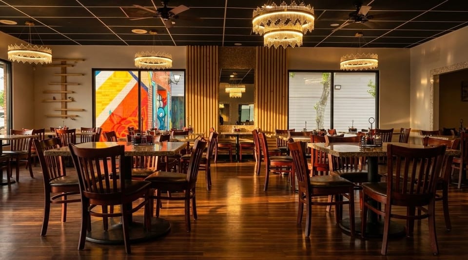 An empty restaurant dining room with wooden chairs, granite tables, and ornate chandeliers.